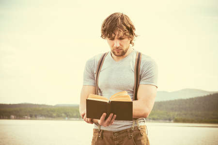 Young Man reading book standing outdoor with mountains on background Summer vacations and Lifestyle conceptの写真素材