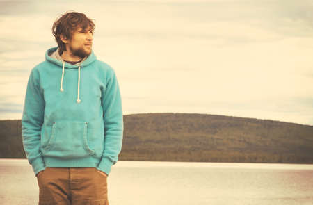 Young Man hipster standing alone outdoor with mountains and lake on background Lifestyle and melancholy emotions conceptの写真素材