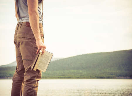 Young Man with book outdoor lake on background Summer vacations and Lifestyle conceptの写真素材