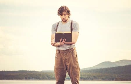 Young Man reading book standing outdoor with mountains on background Summer vacations and Lifestyle conceptの写真素材