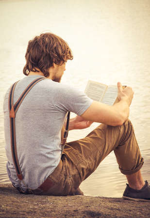 Young Man reading book outdoor with lake on background Summer vacations and Lifestyle conceptの写真素材