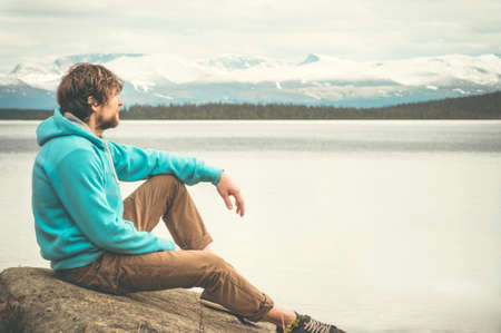 Young Man relaxing alone outdoor Lifestyle Travel concept scandinavian mountains and lake on backgroundの写真素材