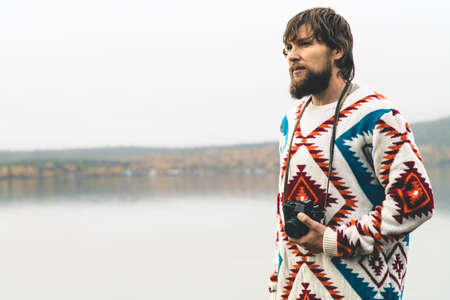 Young Man bearded with retro photo camera Fashion Travel Lifestyle wearing knitted sweater clothing outdoor foggy nature on backgroundの写真素材