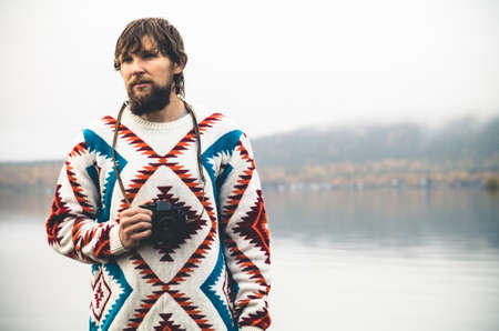 Young Man bearded with retro photo camera Fashion Travel Lifestyle wearing knitted sweater clothing outdoor foggy nature on backgroundの写真素材