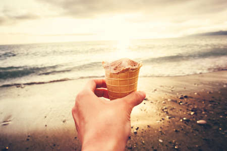 Hand holding Ice Cream with sea beach sunset on background Summer vacations Travel Lifestyle conceptの写真素材