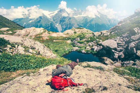 Man laying relaxing with backpack on rocks Travel Lifestyle concept serene view of mountains landscape summer vacations outdoor の写真素材