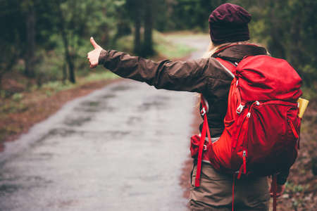 Hitchhiker with red backpack alone on the road Travel Lifestyle concept rear viewの写真素材
