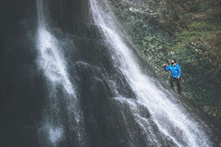 Man Traveler climbing on waterfall rocks Travel Lifestyle adventure concept extreme vacations survival into the wildの写真素材