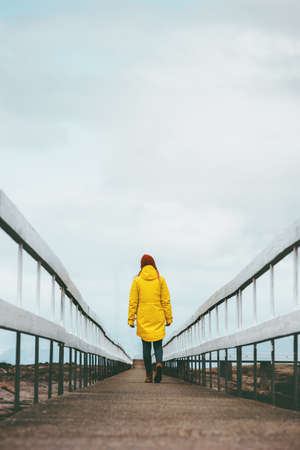 Girl Traveler alone walking away on bridge road Travel Lifestyle emotional concept vacations outdoor yellow raincoat clothingの写真素材