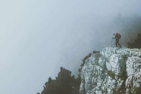 Traveler on foggy cliff mountains with backpack Travel Lifestyle success motivation concept adventure active vacations outdoorの写真素材