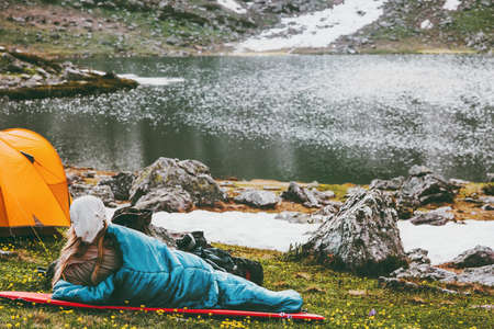 Woman relaxing in sleeping bag on mat enjoying lake landscape Travel Lifestyle camping concept adventure summer vacations outdoor hiking harmony with natureの写真素材