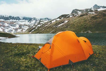Orange camping tent at lake in mountains landscape Travel Lifestyle concept adventure summer vacations outdoor hiking gear equipmentの写真素材