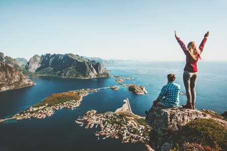 Couple family traveling together on cliff edge in Norway man and woman lifestyle concept summer vacations outdoor aerial view Lofoten islands Reinebringen mountain topの写真素材