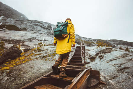 Traveler woman climbing up stairs in scandinavian mountains Traveling alone adventure Lifestyle active vacations in Norway girl wearing yellow raincoat with backpackの写真素材
