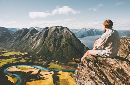 Man sitting on cliff edge relaxing with aerial mountains landscape Travel lifestyle adventure vacations in Norway traveler thinking aloneの写真素材