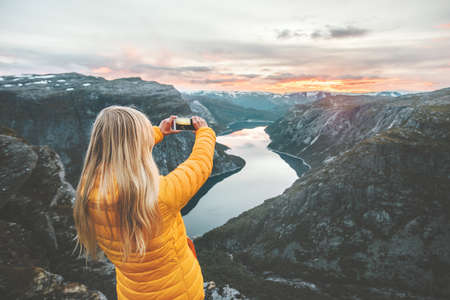 Woman tourist taking photo by smartphone on mountain top traveling in Norway adventure lifestyle active vacations modern technology connection conceptの写真素材