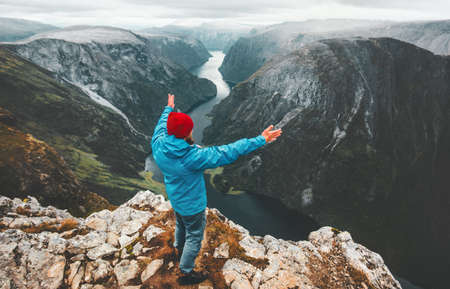 Brave traveler man raised hands traveling in Norway standing on cliff mountain active lifestyle weekend getaway adventure vacations success concept aerial Naeroyfjord landscapeの写真素材