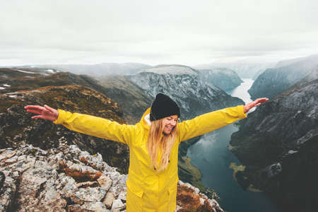 Happy girl traveling in mountains success raised hands healthy active lifestyle adventure vacations aerial Norway fjord view girl wearing yellow raincoat scandinavian tripの写真素材
