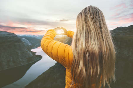 Woman traveling in sunset mountains hands heart symbol shaped Lifestyle emotional concept vacations weekend getaway aerial Norway landscape  の写真素材