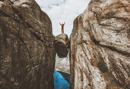 Brave woman traveler standing on Kjeragbolten raised hands Traveling in Norway Kjerag mountains summer vacations adventure success conceptの写真素材