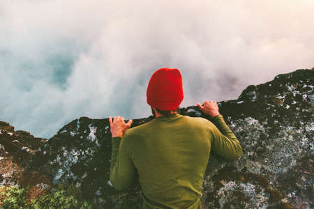 Man lying down on the edge cliff above clouds gaze into abyss mountains travel adventure lifestyle extreme vacationsの写真素材