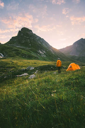 Camping in mountains man alone enjoying sunset landscape Travel adventure lifestyle concept active summer vacations with tent in wildernessの写真素材