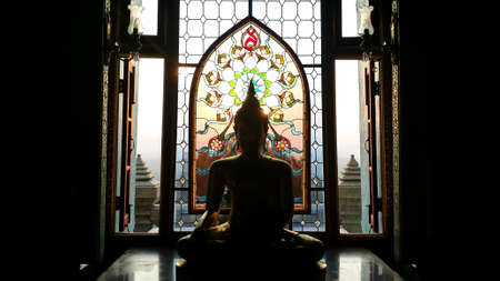 Silhouette buddha statue has flower and sun pattern stained glass is background,  Wat Pramahathadchedipakdeeprakad  Prachuapkhirikhan Thailand, Historical place and Public place.のeditorial素材