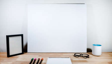 My workspace with white canvas, note book, colorful pens, picture frame, eyeglasses and a coffee cup on wooden desk for new idea and inspiration.の写真素材