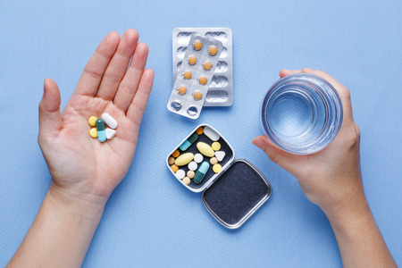 Taking pill with hand holding pills and glass of waterの写真素材