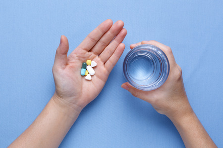 Taking pill with hand holding pills and glass of waterの写真素材