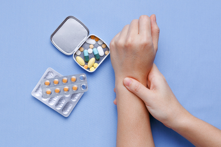 Woman hand with wrist pain and pills on tableの写真素材