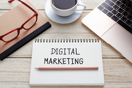 Digital marketing handwriting note with laptop, pencil on notebook, eyeglasses and coffee cup on deskの写真素材