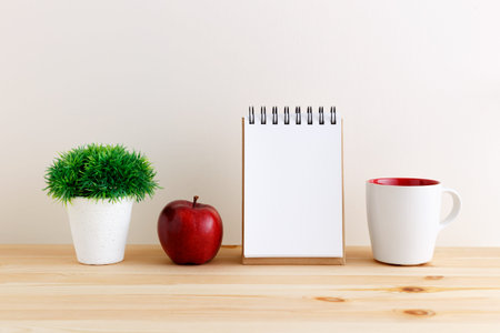 White coffee mug with apple and blank notepad on wooden table