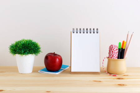 Blank notepad with apple and stationary in cup on wooden tableの写真素材