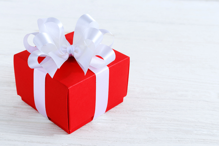Red gift box with white ribbon on white wood tableの写真素材