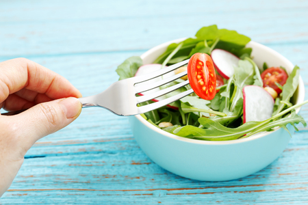 Healthy eating with salad closeup tomato with hand holding forkの写真素材