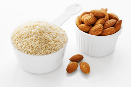 Almond flour in measuring cup with almonds on white backgroundの写真素材