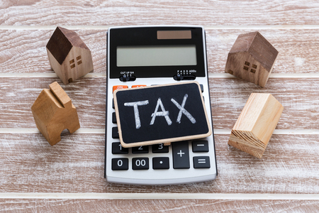 Tax sign on calculator with house model on wooden tableの写真素材