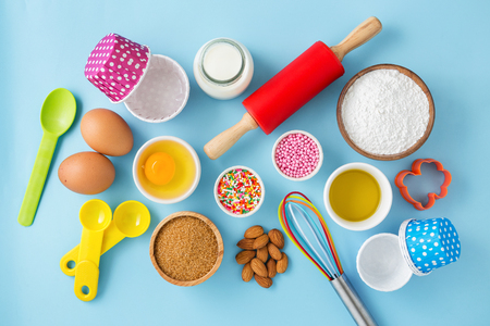 Baking cupcake with ingredients eggs, flour, milk, sugar, olive oil, almond, cake decor and kitchen tools on light blue table from top viewの写真素材