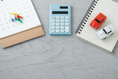 Calculator and toy cars with calendar and pins on wooden table backgroundの写真素材