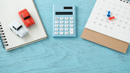 Calculator and toy cars with calendar and pins on blue wooden backgroundの写真素材