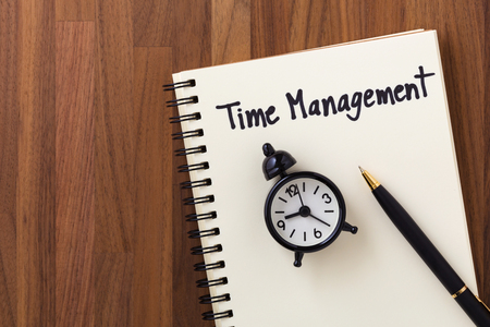 Time management concept with notebook, clock and pen on wooden table from top viewの写真素材