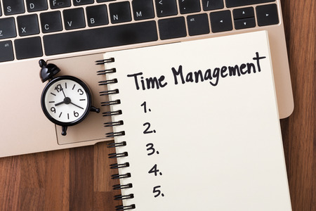 Time management concept with list on notebook and clock on computer from top viewの写真素材