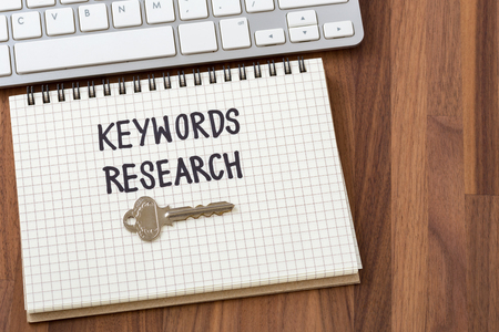 Keywords research words on notebook with key and computer keyboardの写真素材