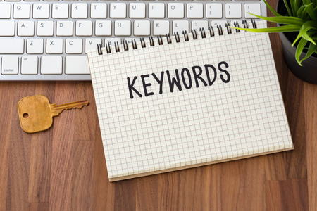 Keywords word on notebook with key and computer on wooden tableの写真素材