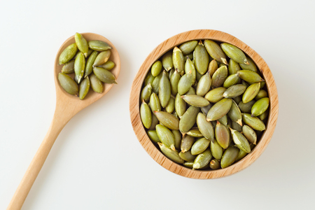 Pumpkin seeds in wooden bowl and spoon on white background, top viewの写真素材
