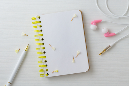 Earphones and notebook with pen on white desk, top viewの写真素材