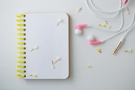 Earphones and notebook with flower on white wooden table backgroundの写真素材