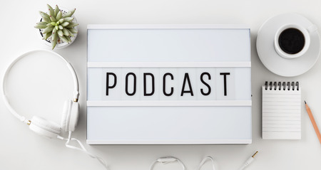 Podcast word on lightbox with headphones, coffee cup and notepad on white background, flat layの写真素材