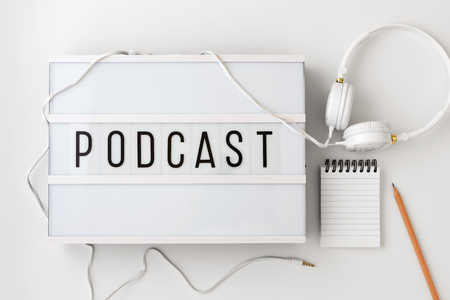 Podcast word on lightbox with headphones, notepad and pencil on white background, podcast concept, flat layの写真素材